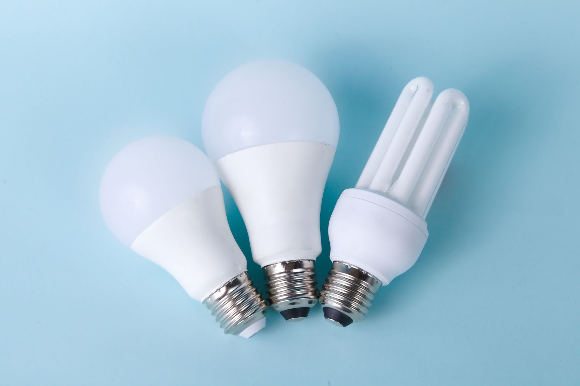 Three assorted LED and CFL light bulbs against a light blue background.