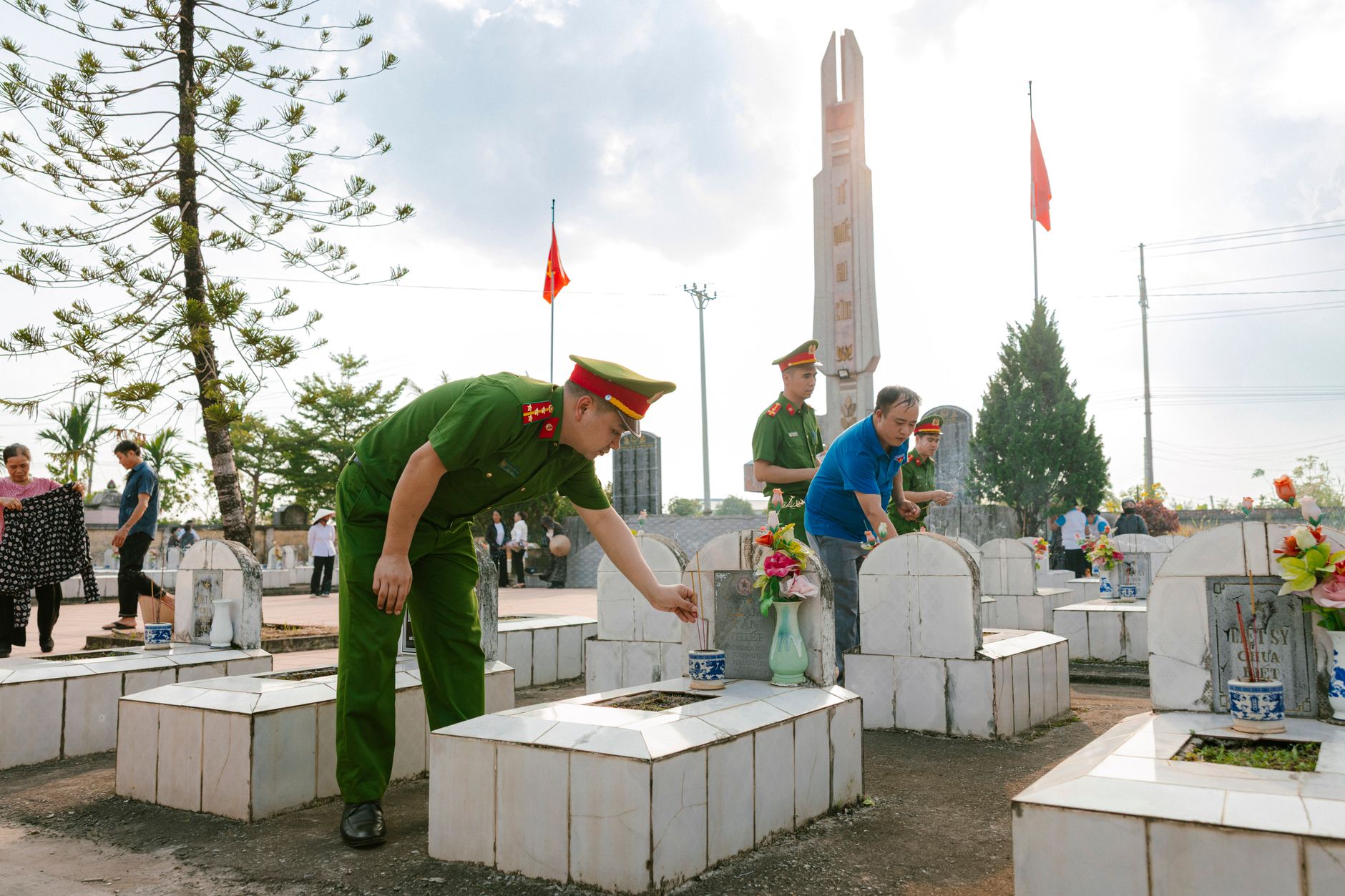 People paying respects at a cemetery, honoring fallen soldiers with flowers and incense.