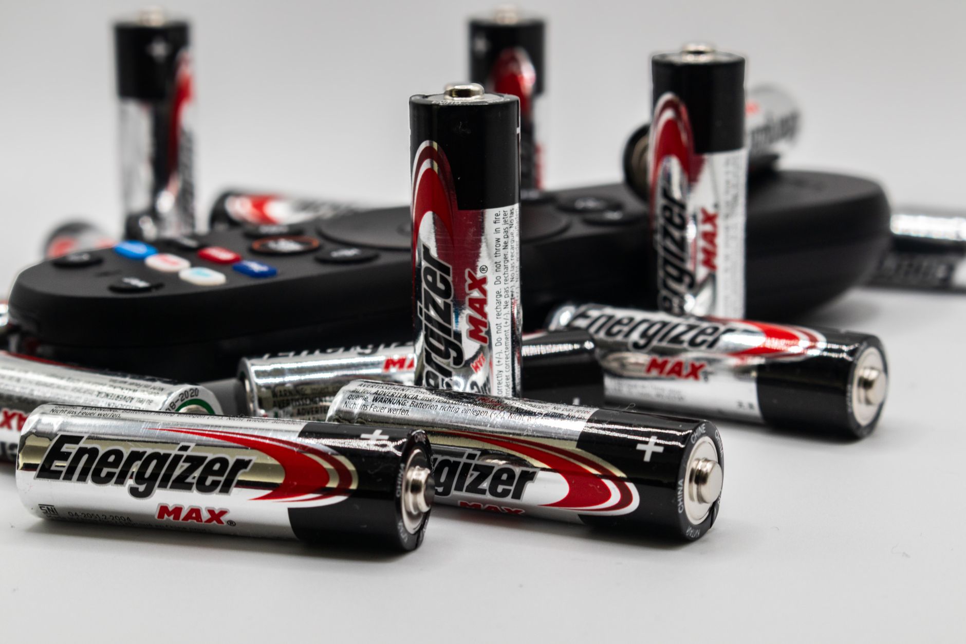 Close-up of multiple Energizer AA batteries and a remote control on a white surface.