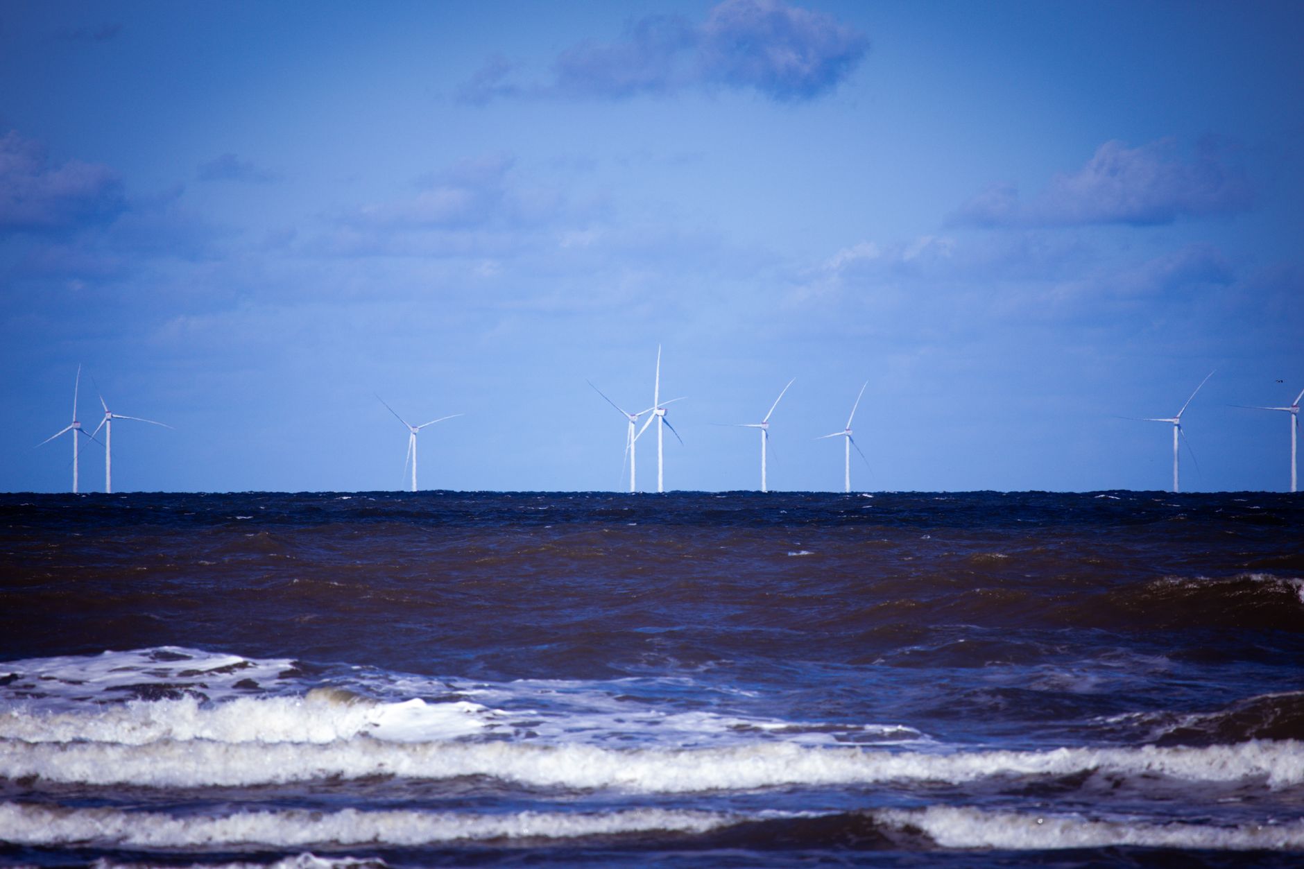 Offshore wind turbines generating sustainable energy over a calm ocean under a clear blue sky.