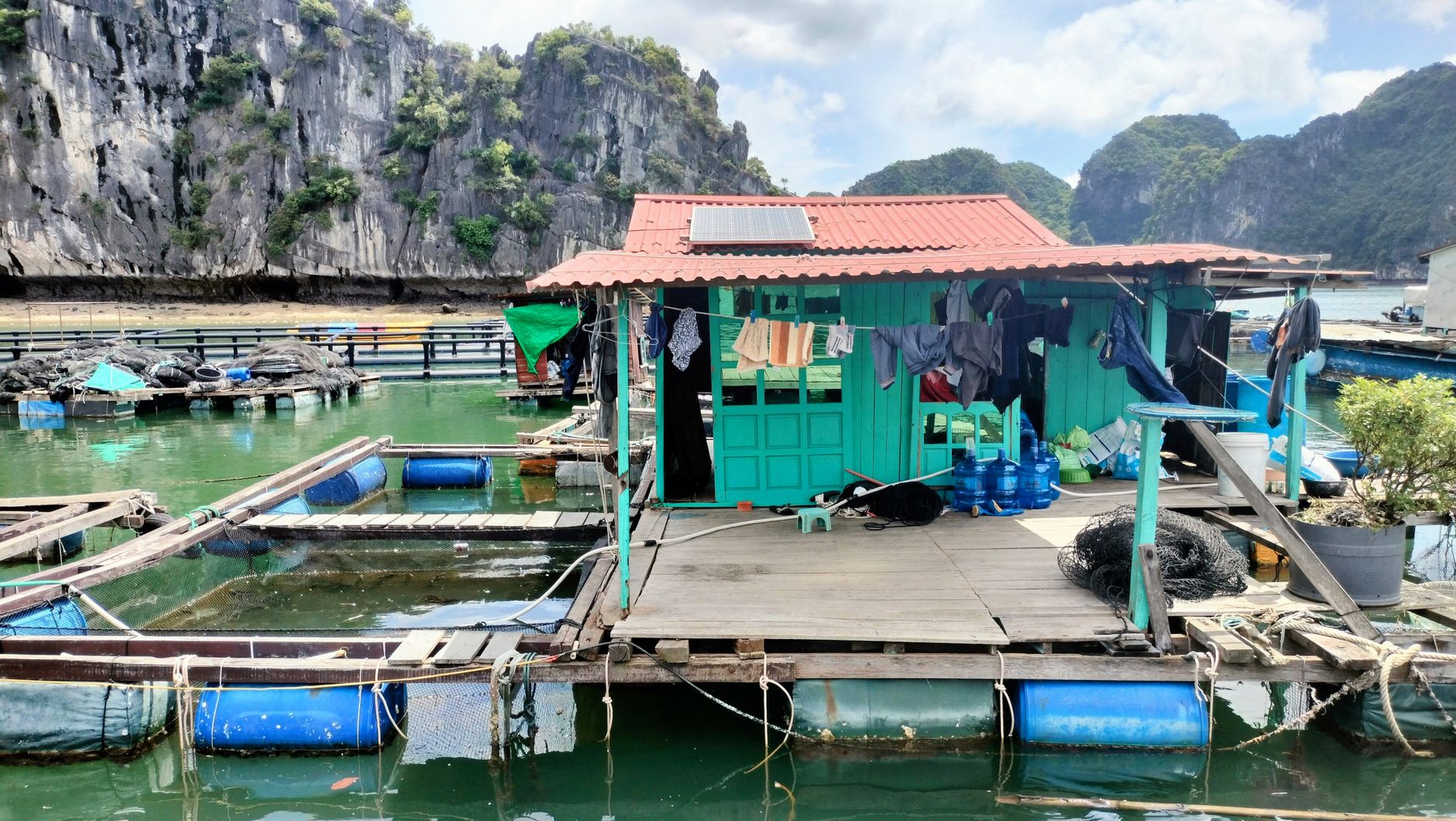 A vibrant floating fish farm with a wooden house and aquaculture cages in Ha Long Bay, Vietnam.