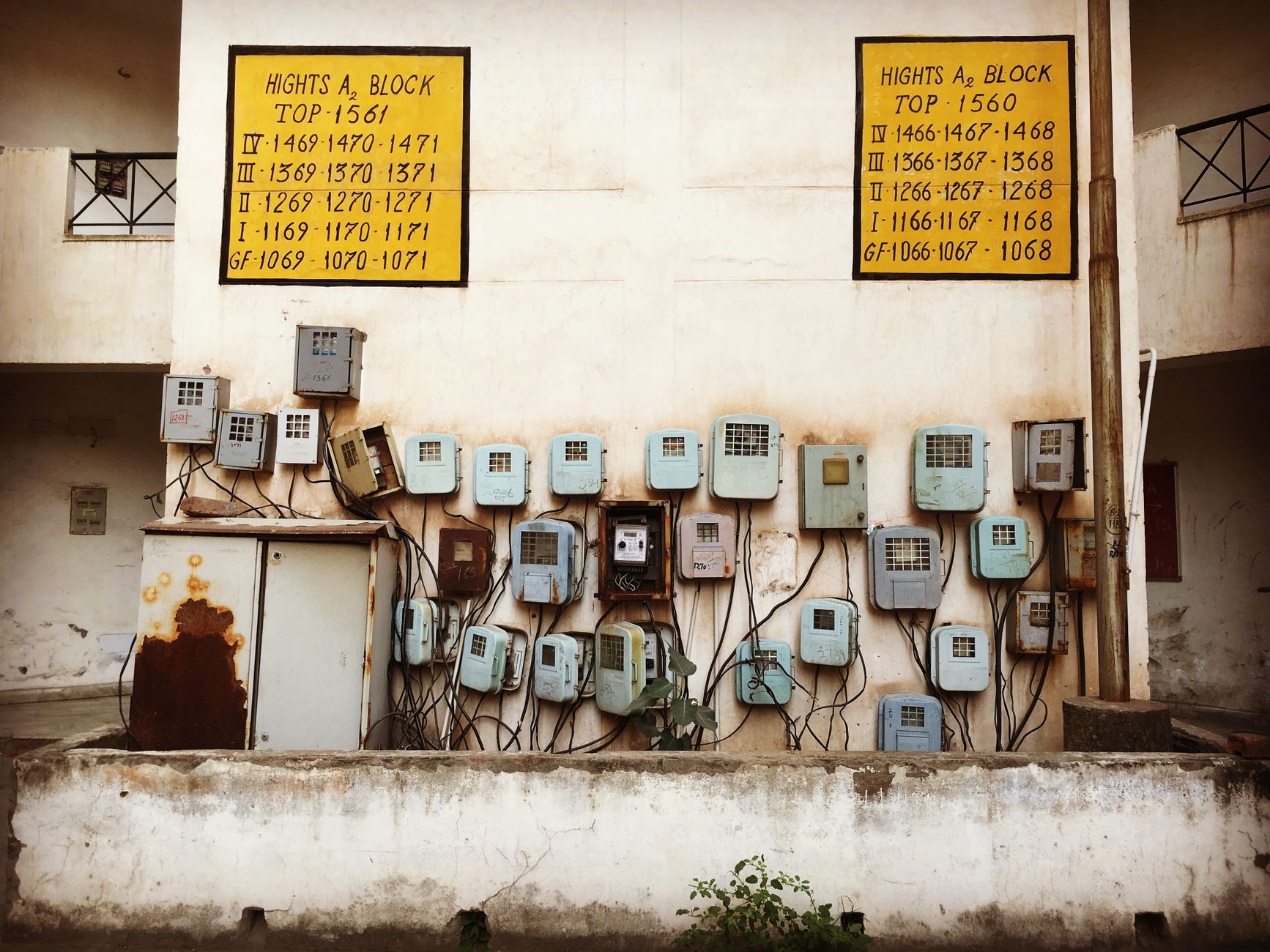 Aged electrical meters and wiring mounted on a concrete wall of an old building in India.