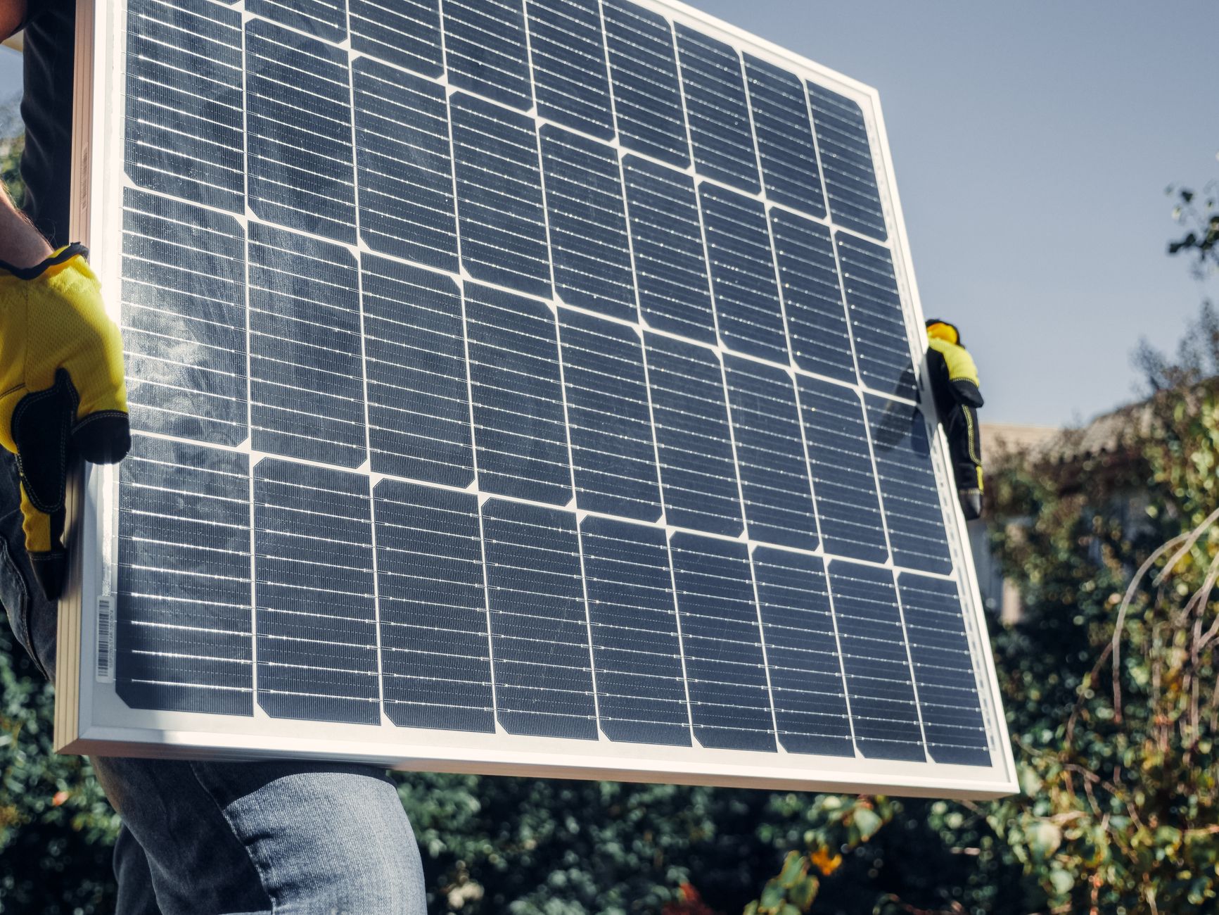 Close-up of technician with safety gear installing a solar panel outdoors.