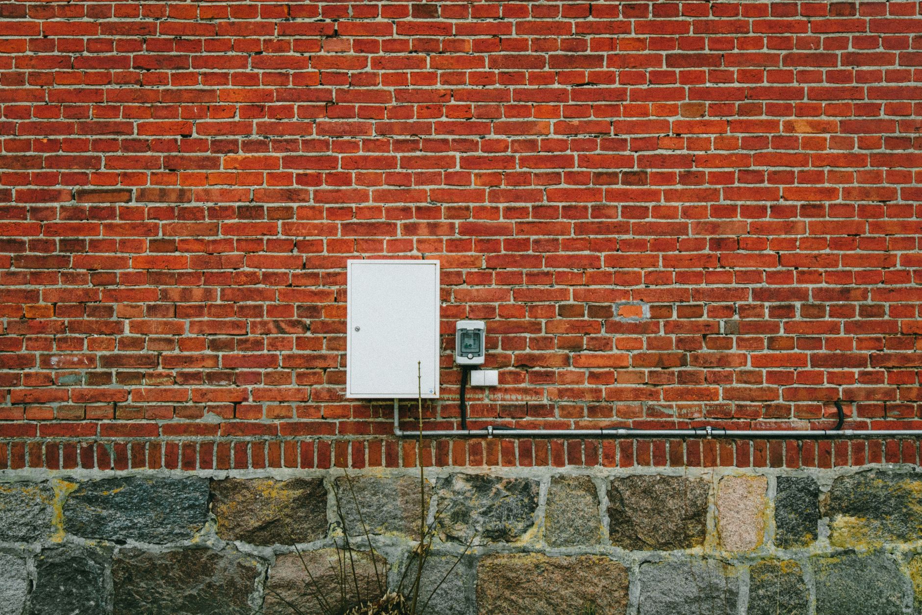 A textured red brick wall with an electric meter box, captured outdoors in Poland.