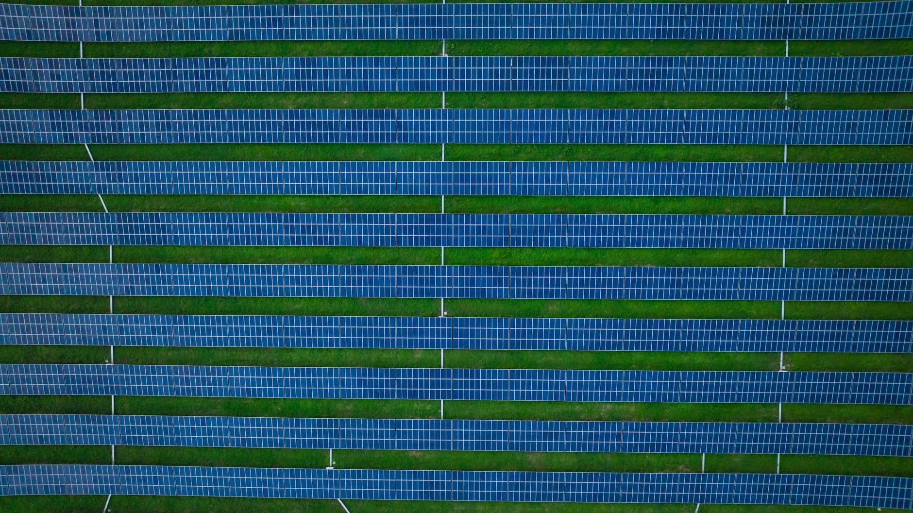 Aerial photograph of a solar farm featuring rows of solar panels and green spaces.