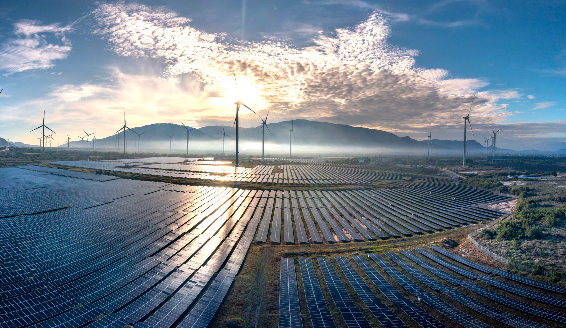 Stunning aerial view of a vast solar farm with wind turbines under a vibrant sunrise sky, showcasing renewable energy.