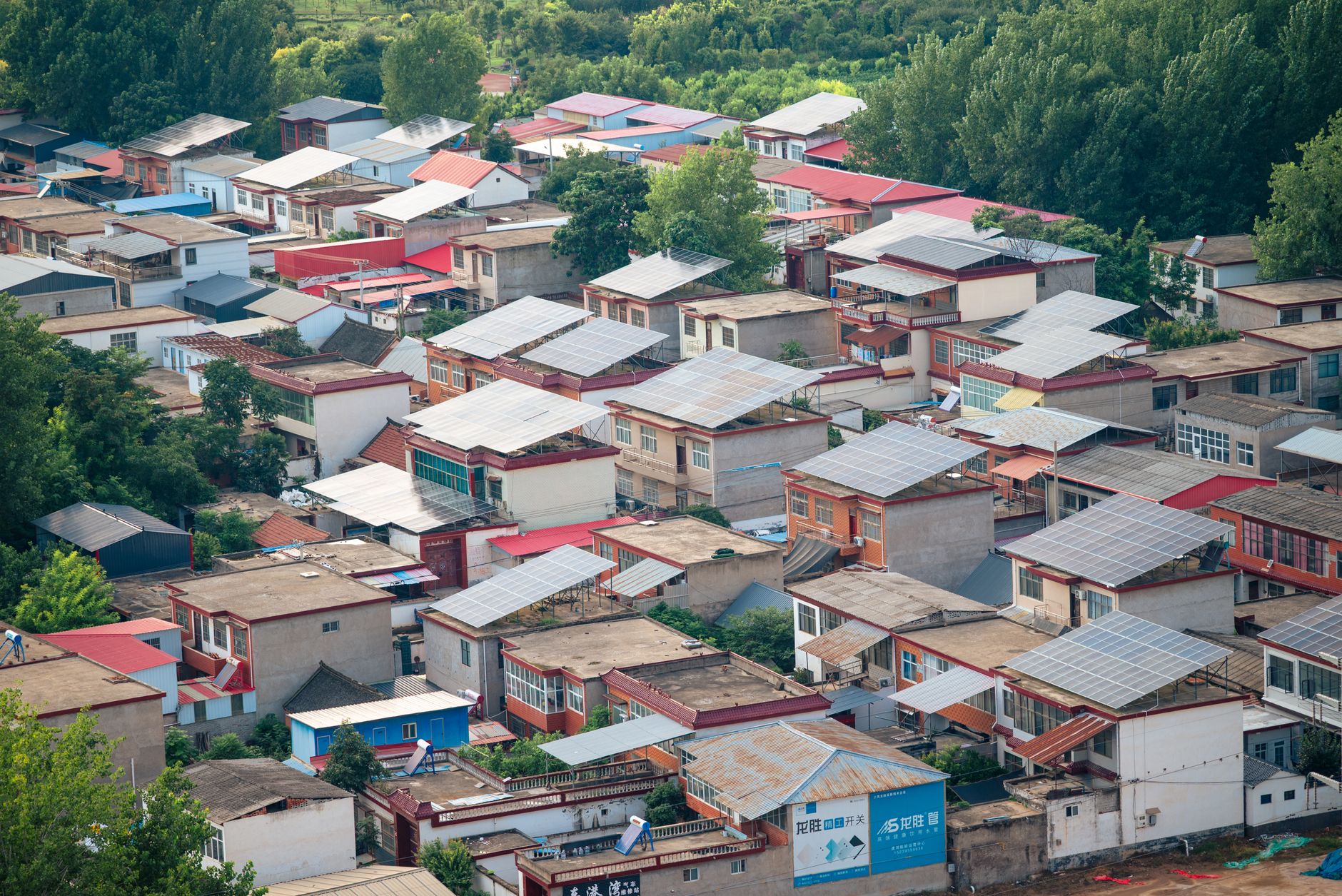 Aerial view showing a residential neighborhood with solar panels on rooftops surrounded by trees.