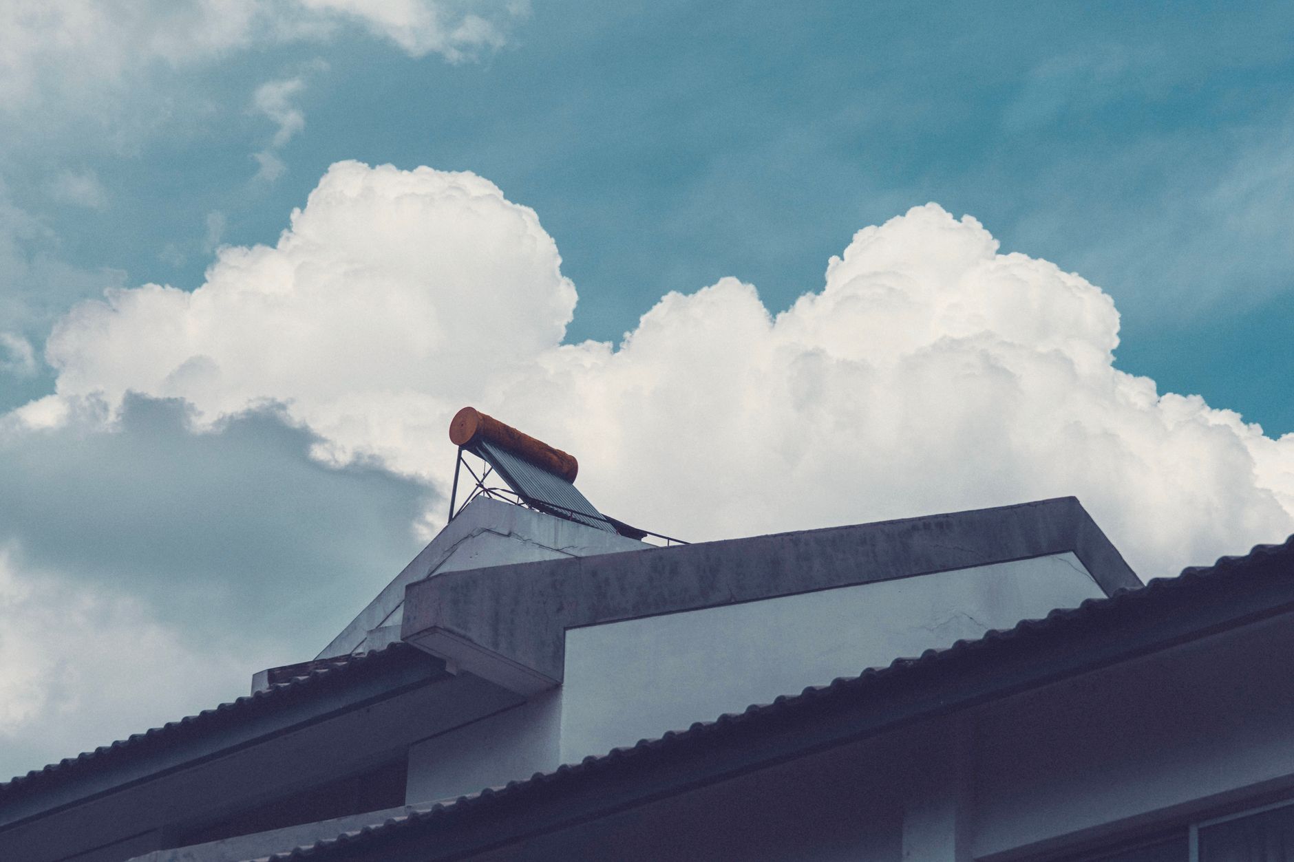 A building rooftop with a solar water heater set against a bright, cloud-filled sky.