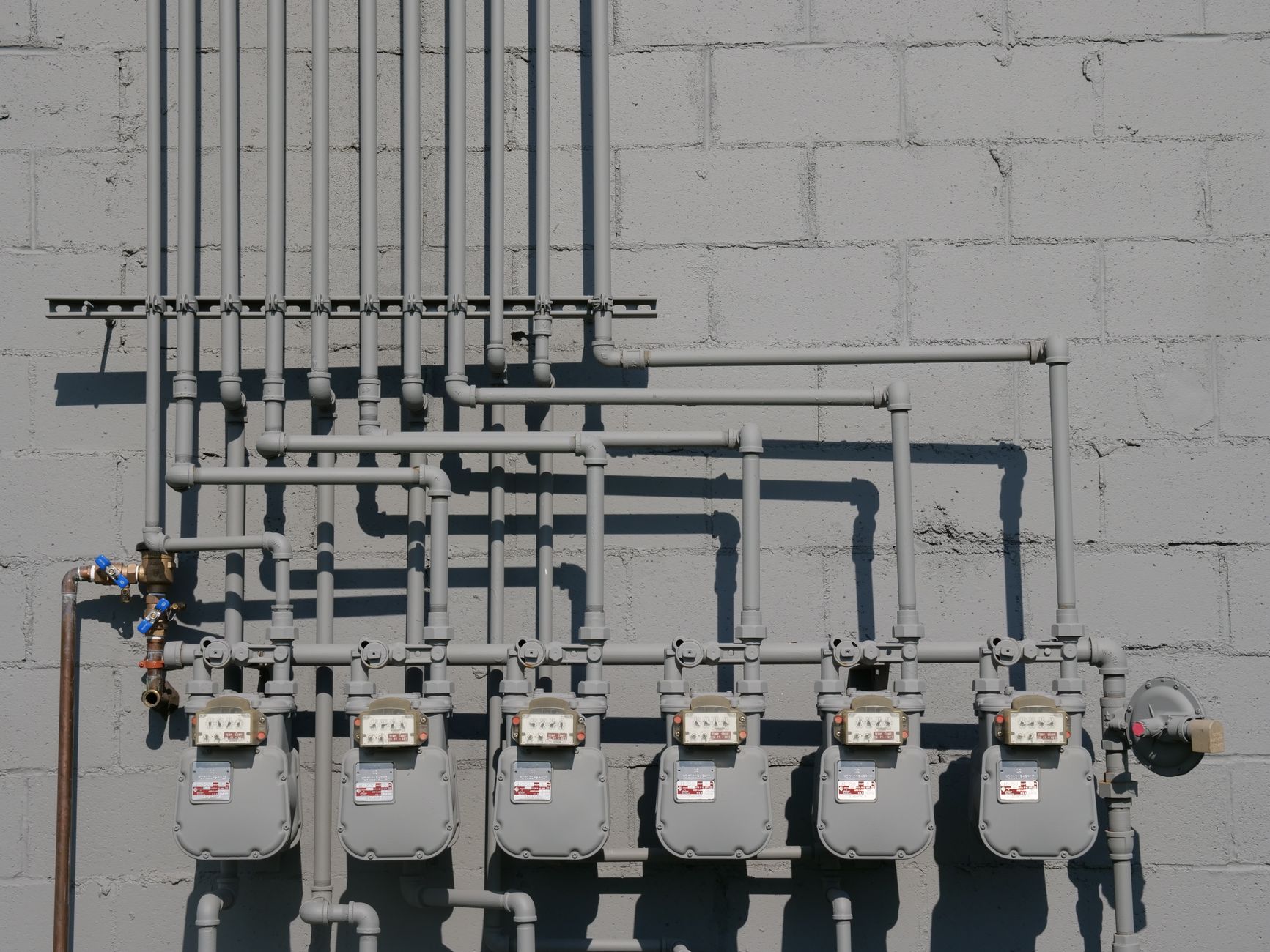 Row of gas meters and piping mounted on a concrete wall, illustrating urban utilities.