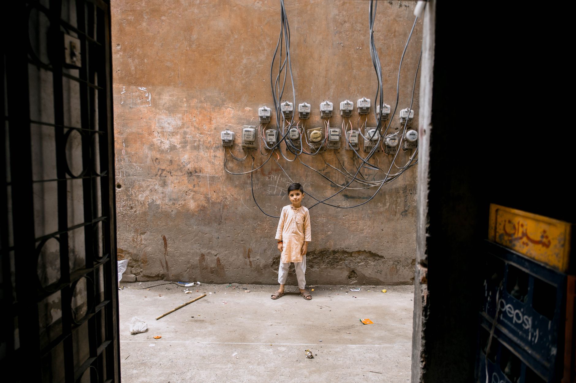 Boy standing in alleyway with electric meters on wall in Faisalabad, Pakistan.