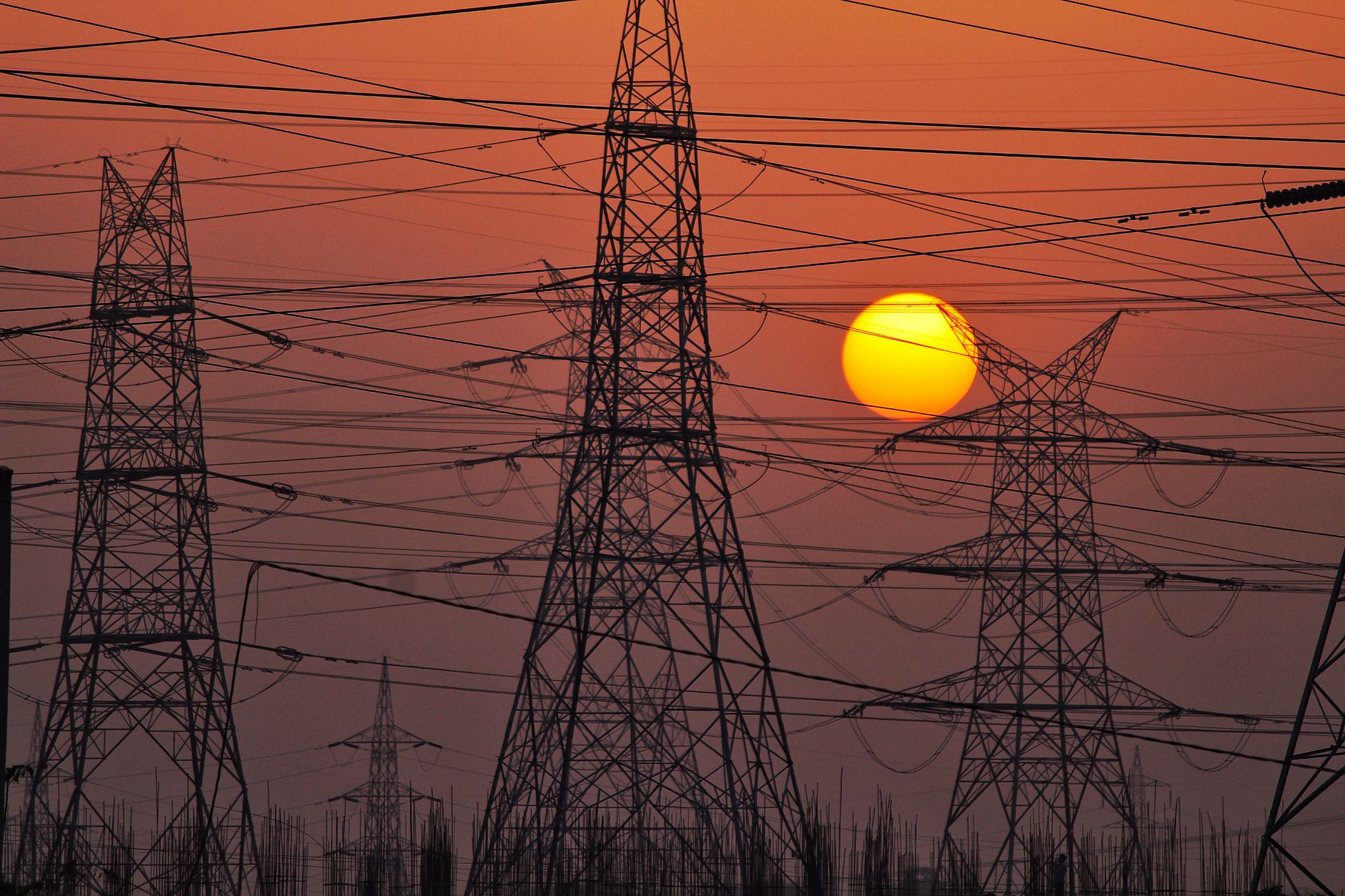 High-tension power lines silhouetted by a dramatic and colorful sunset sky, representing energy distribution.