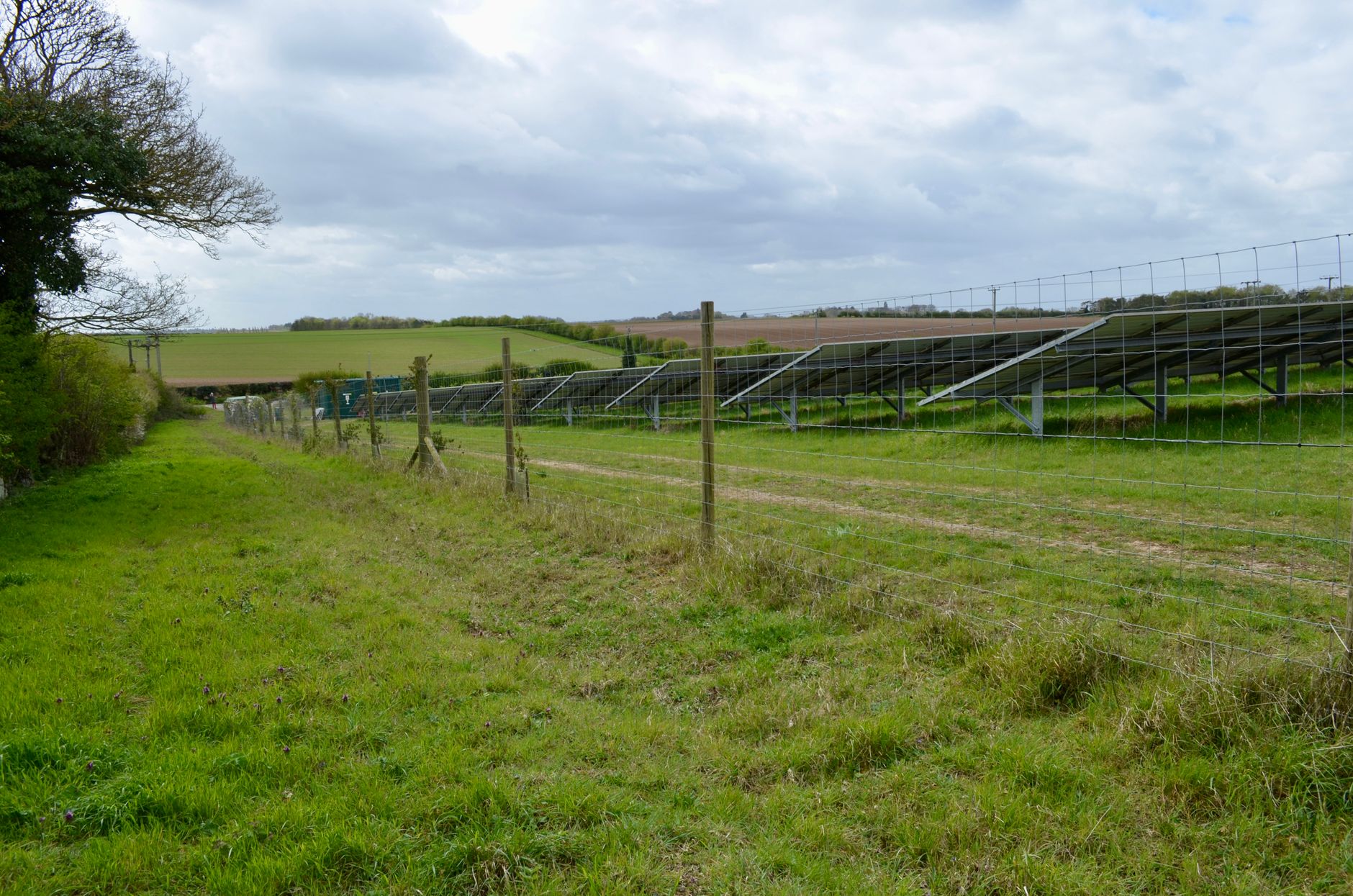Solar panels installed in a rural field landscape under a cloudy sky.