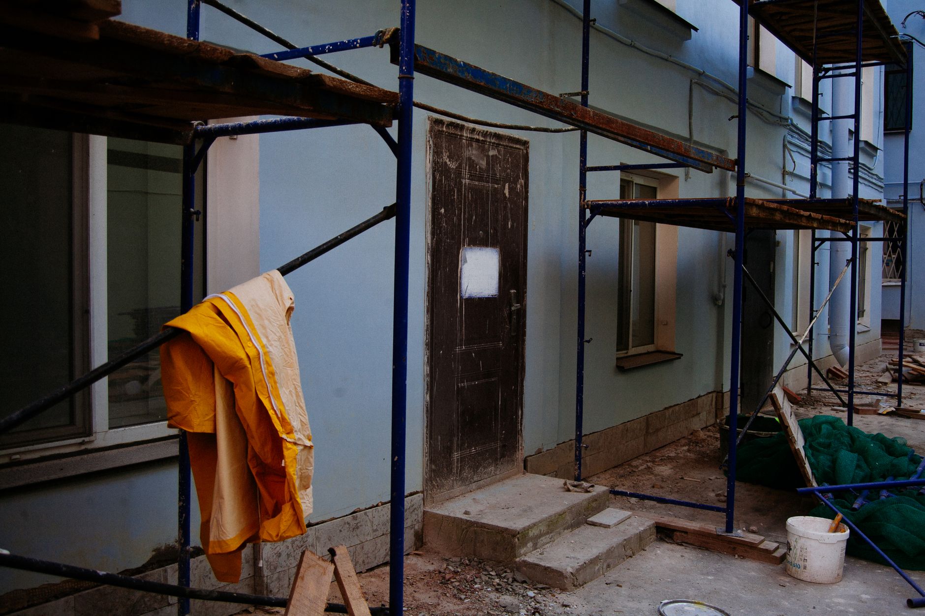 Exterior of renovated house with blue walls and entrance door behind scaffolding with wooden platforms in megapolis