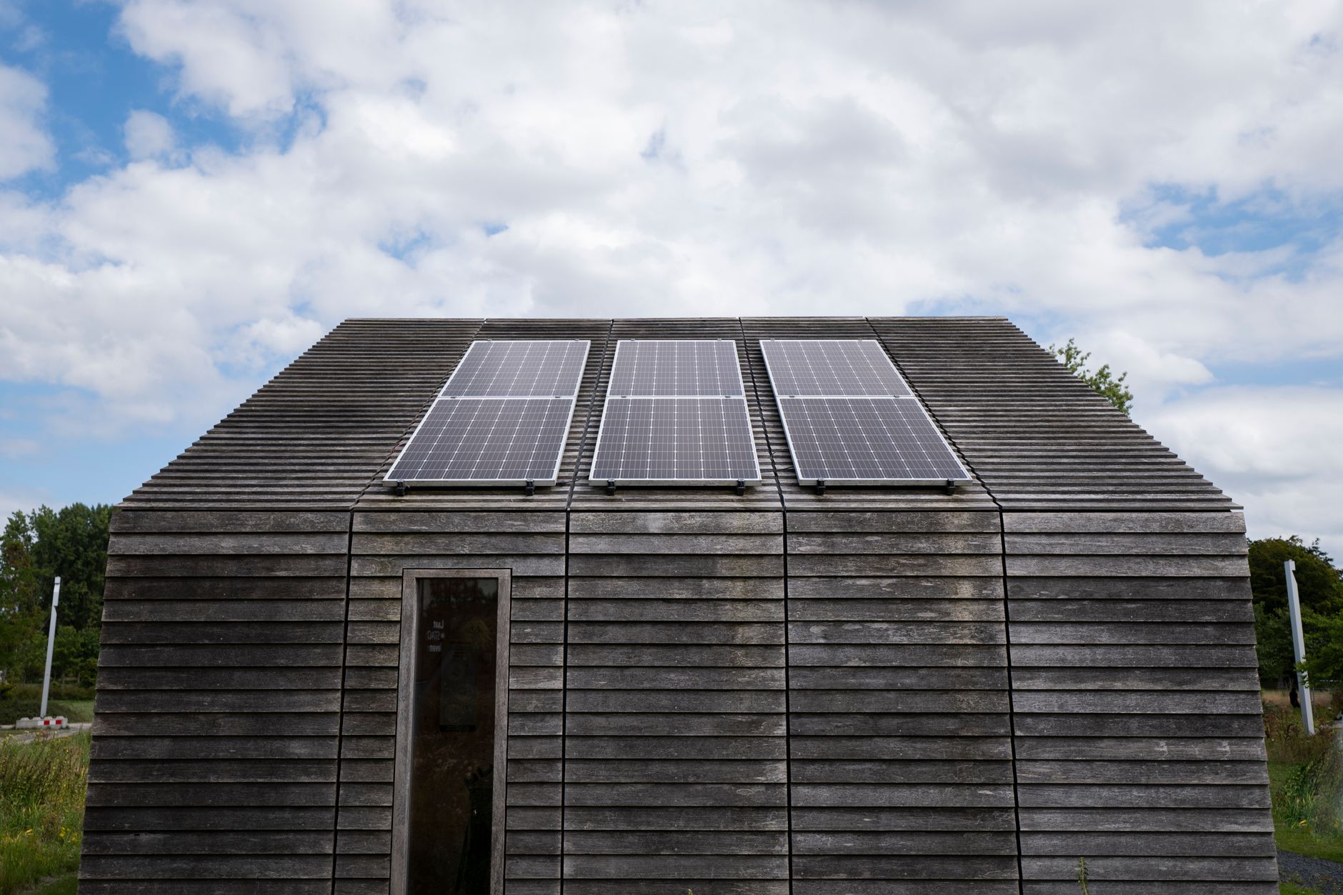 Wooden house with solar panels under a cloudy sky, promoting sustainable energy.
