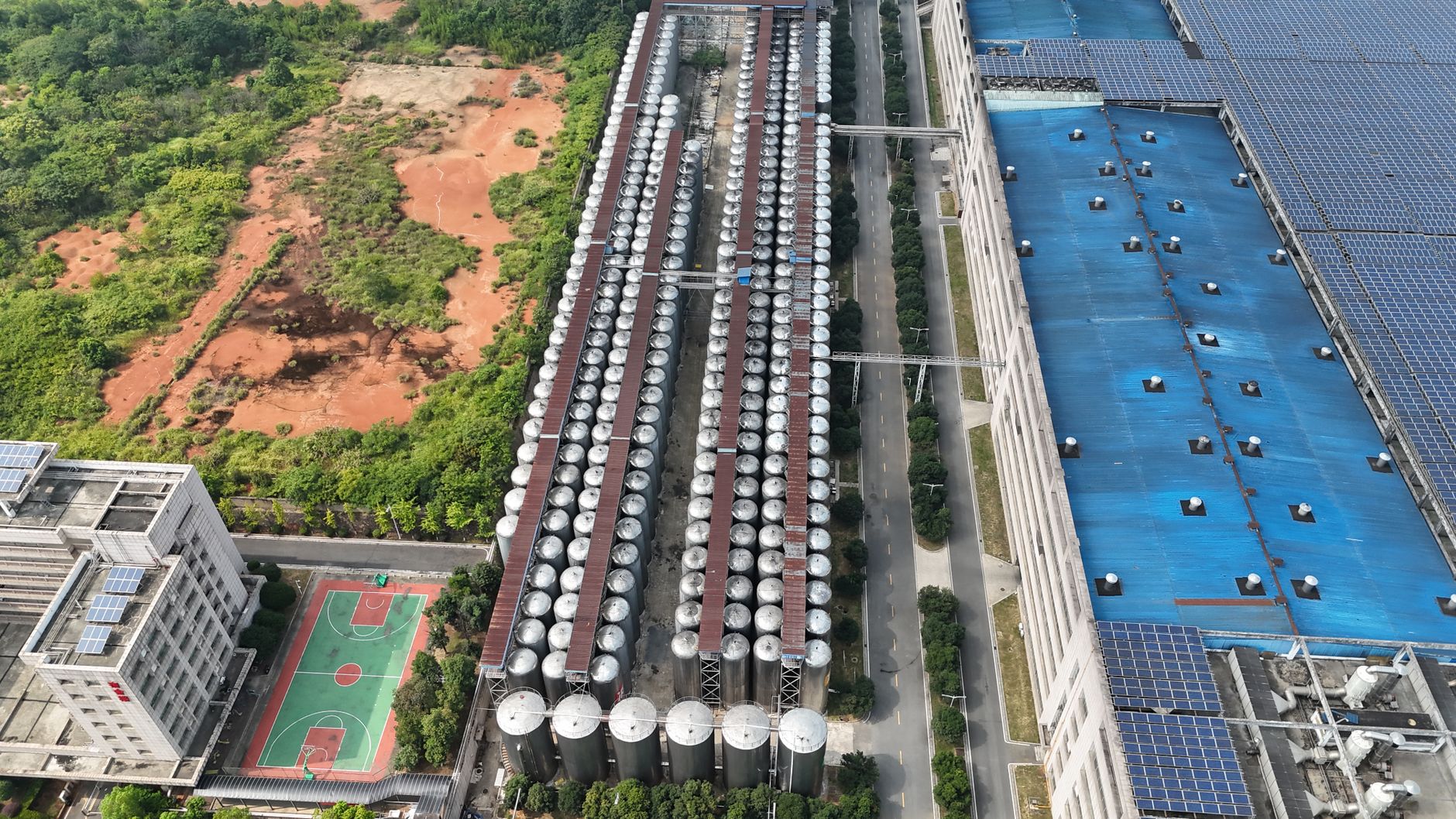 Aerial shot of a factory with solar panels and silos in a green landscape.