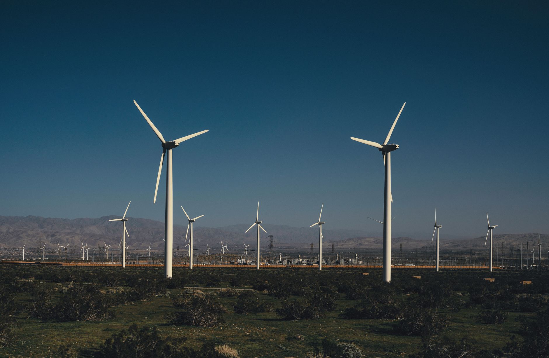 Multiple wind turbines in a vast wind farm capturing renewable energy under a clear blue sky.