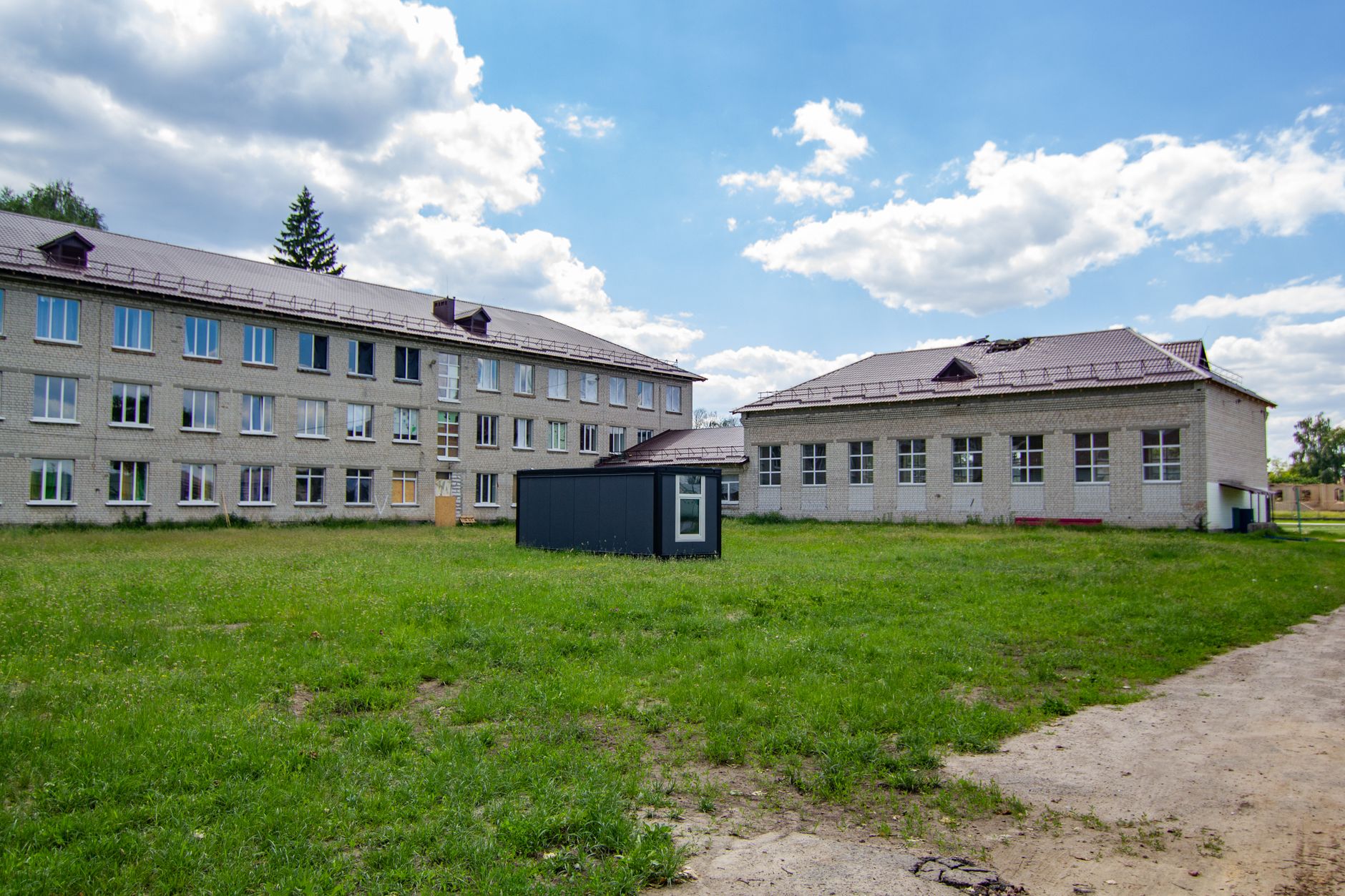 A three-story school structure surrounded by greenery and a clear sky.