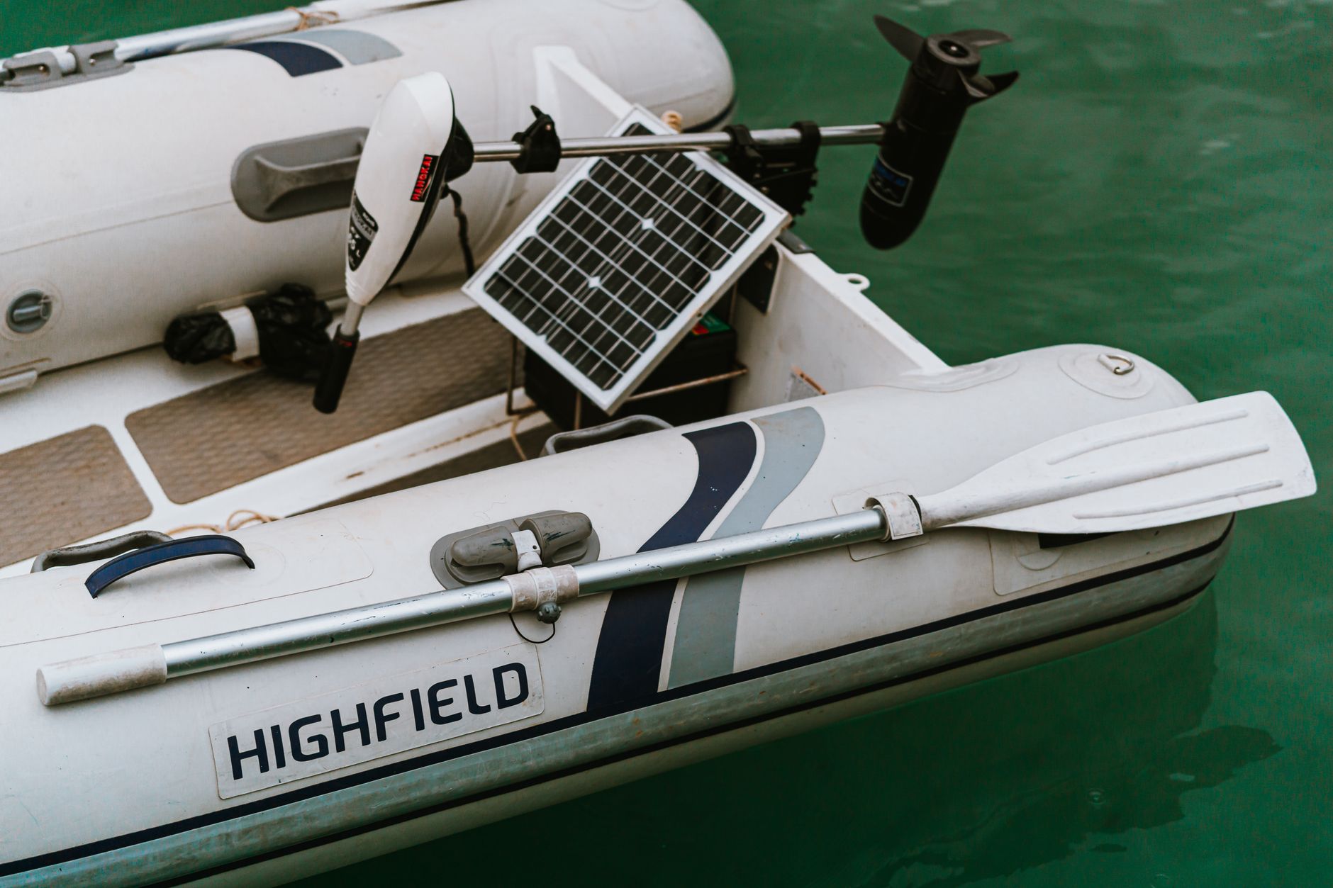 Highfield inflatable boat equipped with a solar panel and paddle, floating on serene waters.