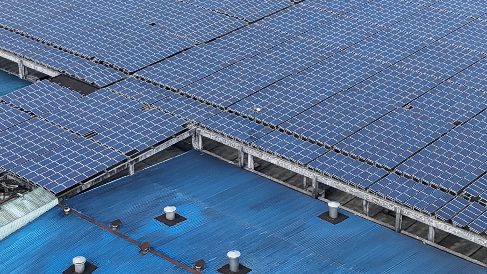 Aerial shot of solar panels installed on a blue industrial rooftop.
