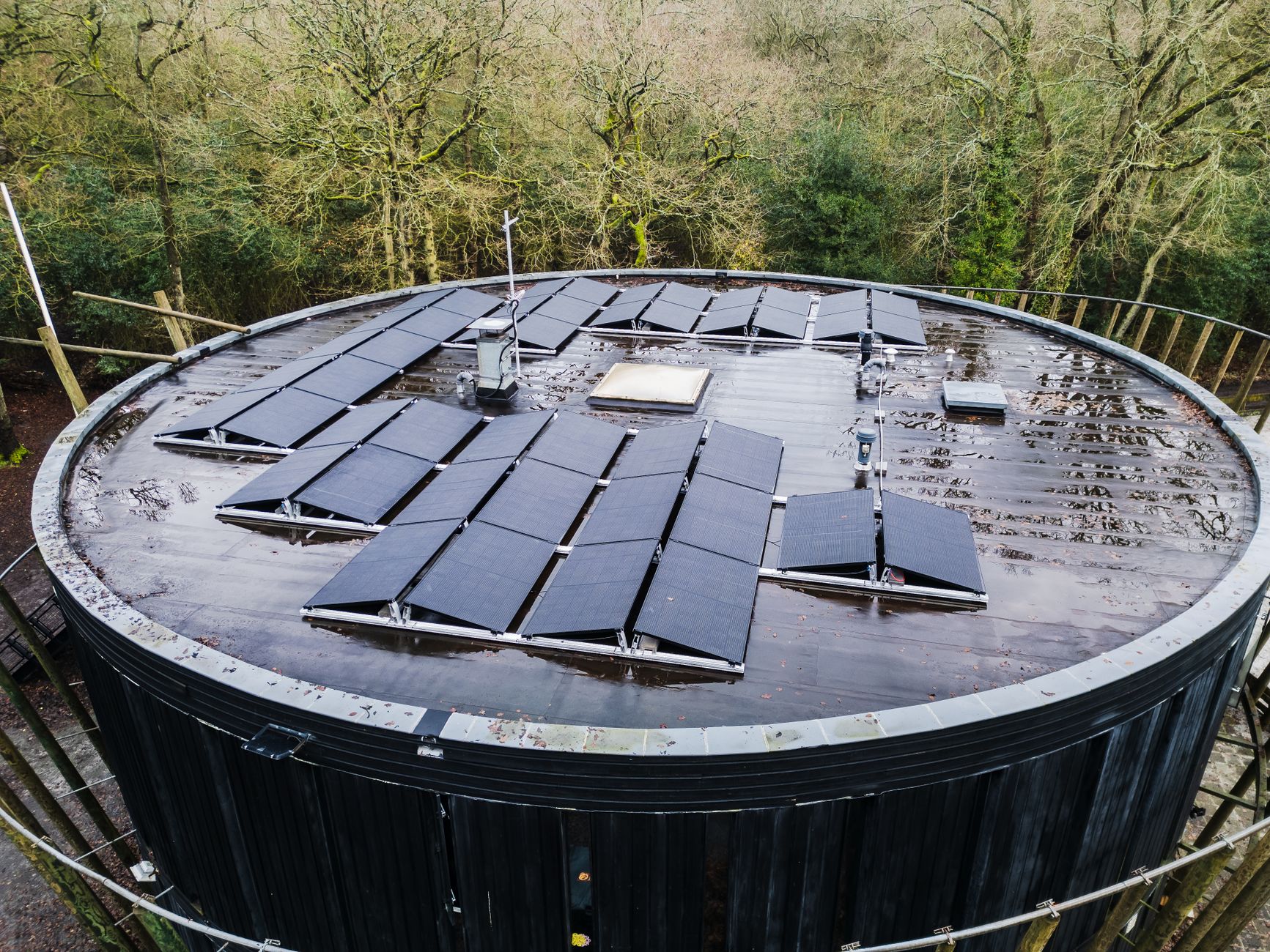 Aerial view of a round rooftop with solar panels surrounded by trees, promoting renewable energy.