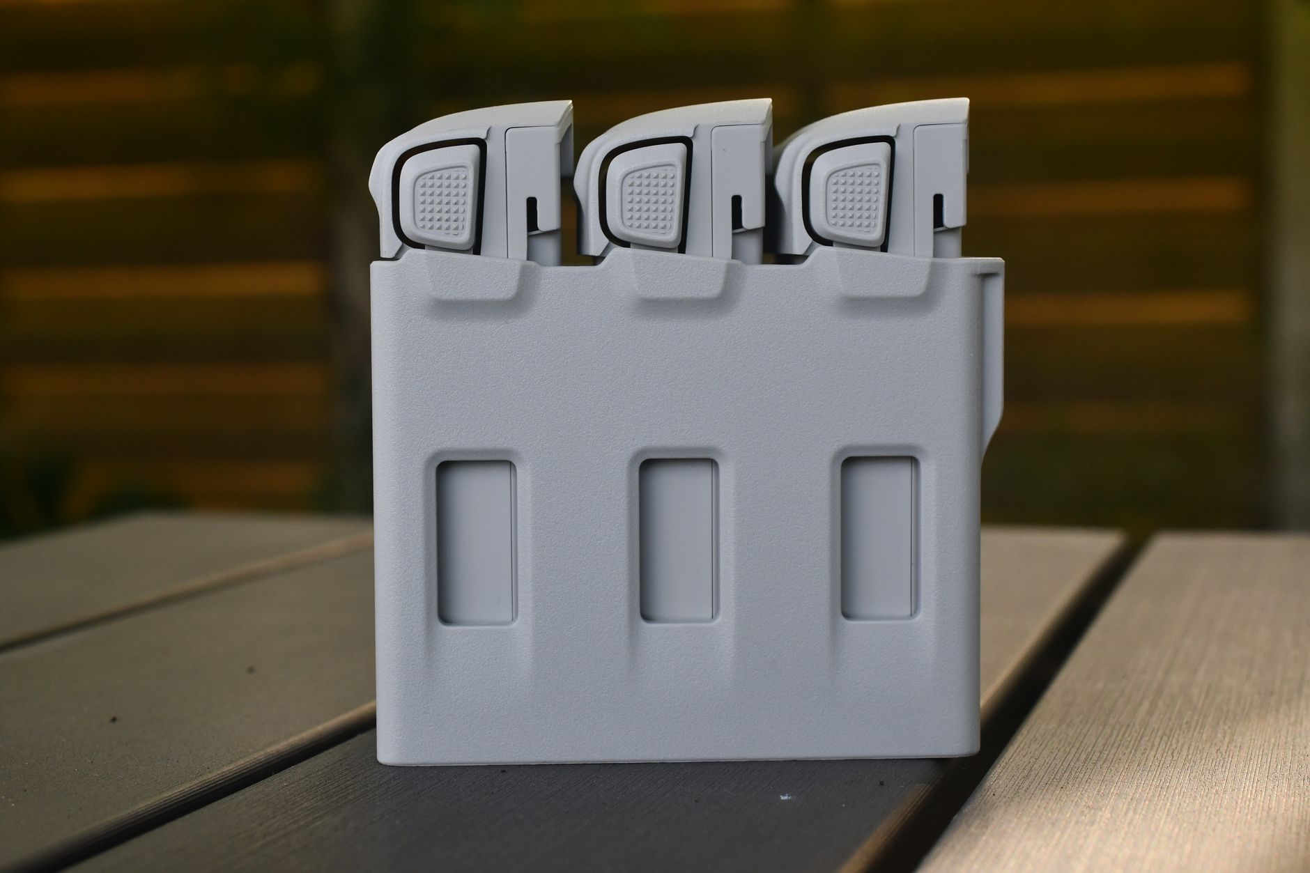 A sleek gray battery storage case with three compartments resting on a wooden outdoor table.
